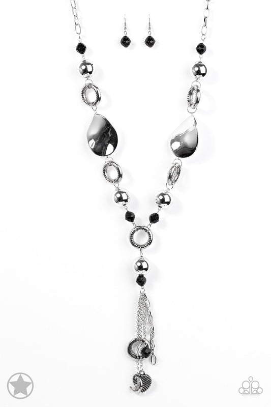 Long chain of black crystalized beads, curved plates of silver with a pearly finish, and chunky silver rings lead down to a tassel of chains and charms, including a crescent moon and a heart.