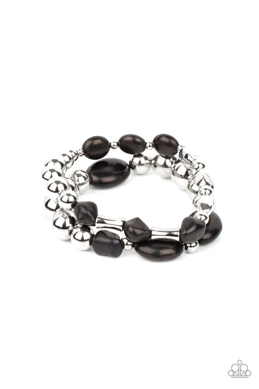 Mismatched black stones and oversized silver beads are threaded along stretchy bands around the wrist, creating earthy layers.