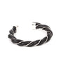 Capped in bold silver fittings, a dainty silver wire and a black leathery cord spin into an edgy cuff around the wrist.