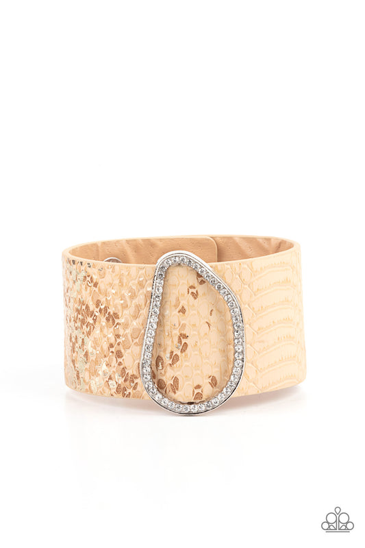 Encrusted with glassy white rhinestones, an asymmetrical silver fitting glides along a tan leather band adorned in a golden metallic python print for a wild look. Features an adjustable snap closure.