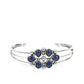A whimsical collection of glassy blue teardrop beads, dainty silver studs, and silver floral accents coalesce into a colorful centerpiece atop a layered silver cuff.