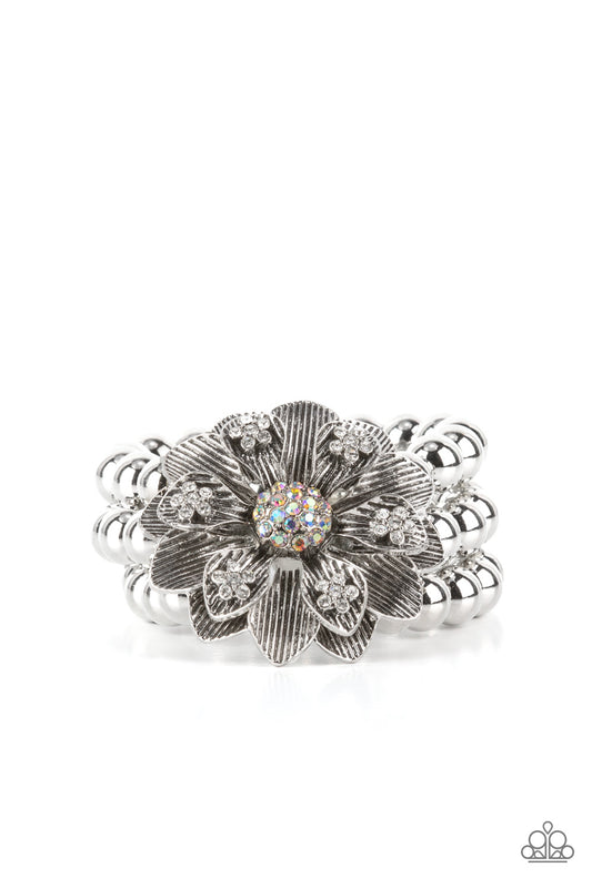 Botanical Bravado--Multi Paparazzi Jewelry       A daring oversized silver flower is composed of petals lined in antiqued silver and dotted with glistening dainty white rhinestones. A sphere of dainty iridescent rhinestones creates the center of the flower as it sits atop a trio of shiny silver beaded stretchy bands around the wrist for a dramatically whimsical look.
