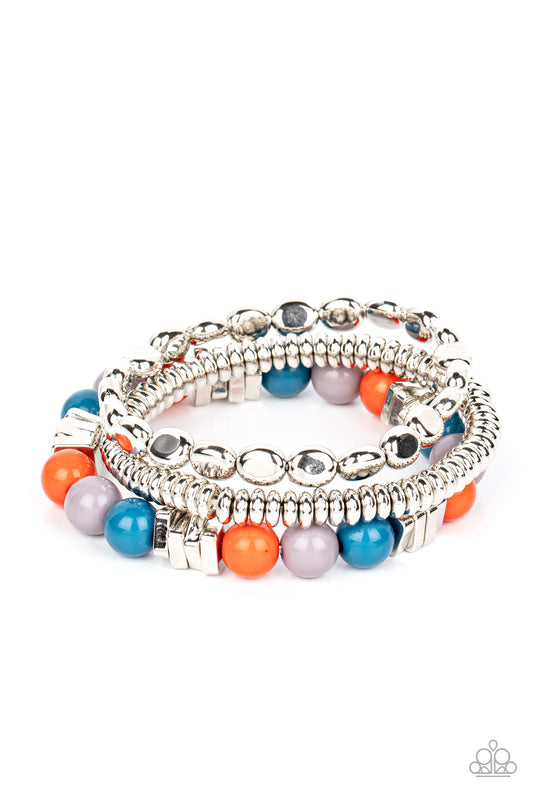 A mismatched collection of silver discs, silver cubes, bubbly multicolored acrylic, and silver pebble-like beads are threaded along stretchy bands around the wrist, creating fiery layers.