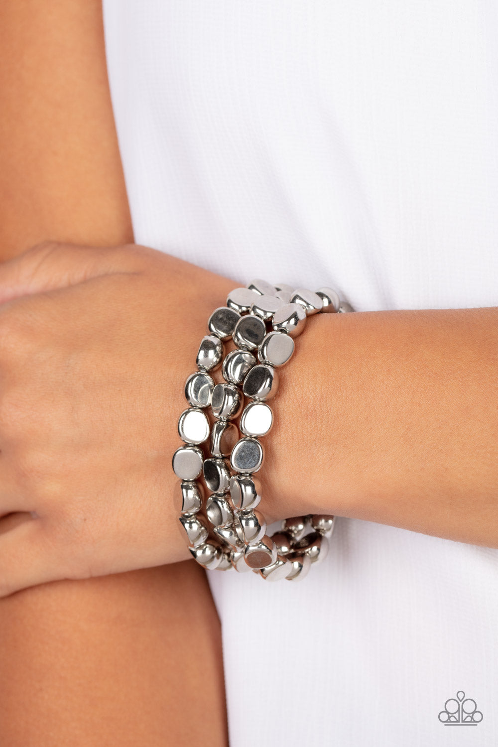 Featuring irregular stone shapes, a shiny series of silver beads are threaded along stretchy bands around the wrist for a bold pop of monochromatic magic.