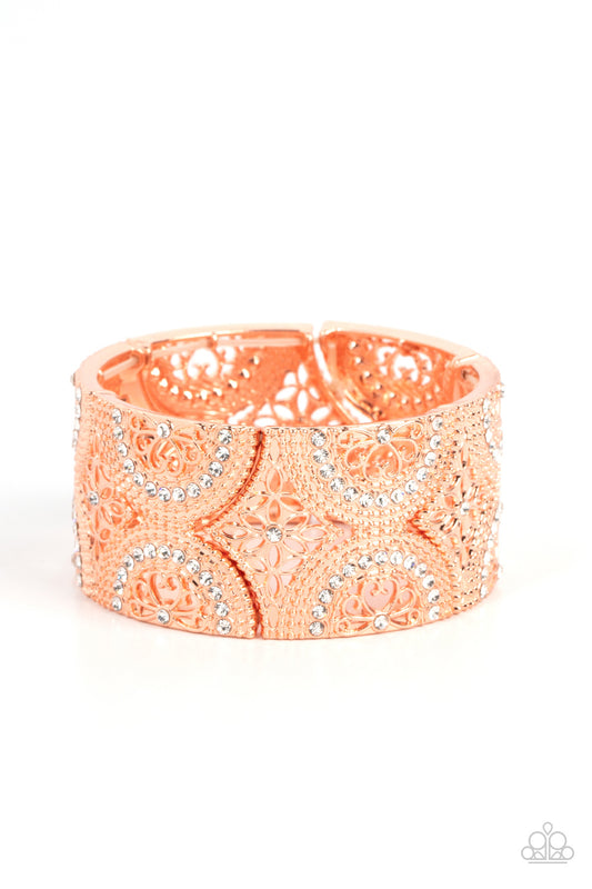 Dotted with sections of glassy white rhinestones, an immaculate display of studded wheel and floral shiny copper patterns combines into shimmering frames along stretchy bands around the wrist for a regal flair.