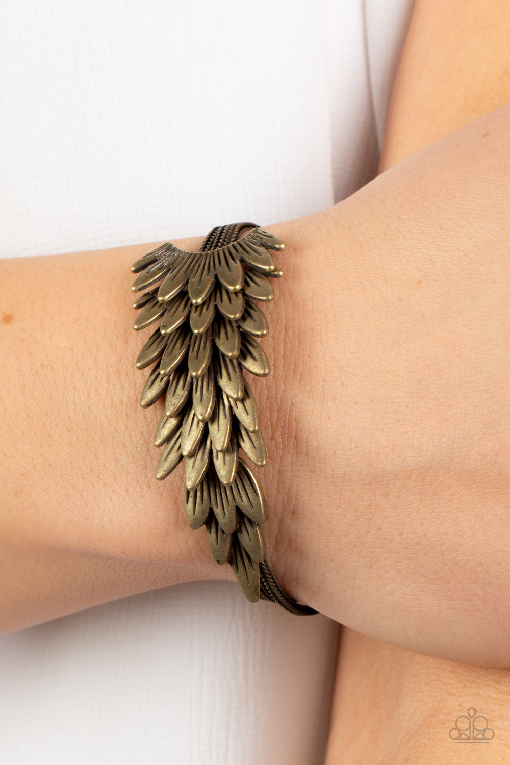 Feathery brass frames delicately overlap across the center of the wrist, creating a boa-like centerpiece atop rows of rustic brass chains. Features an adjustable clasp closure.