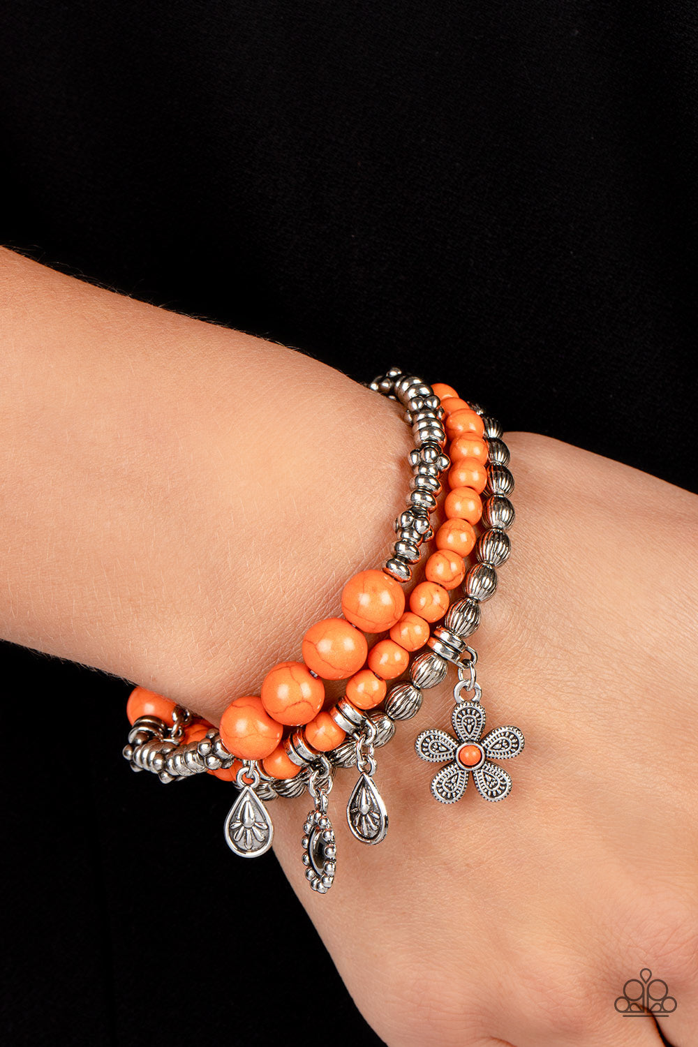 A trio of floral-inspired bracelets, featuring comfortable stretchy bands and smooth orange stones, stack along the wrist to create a bold statement piece
