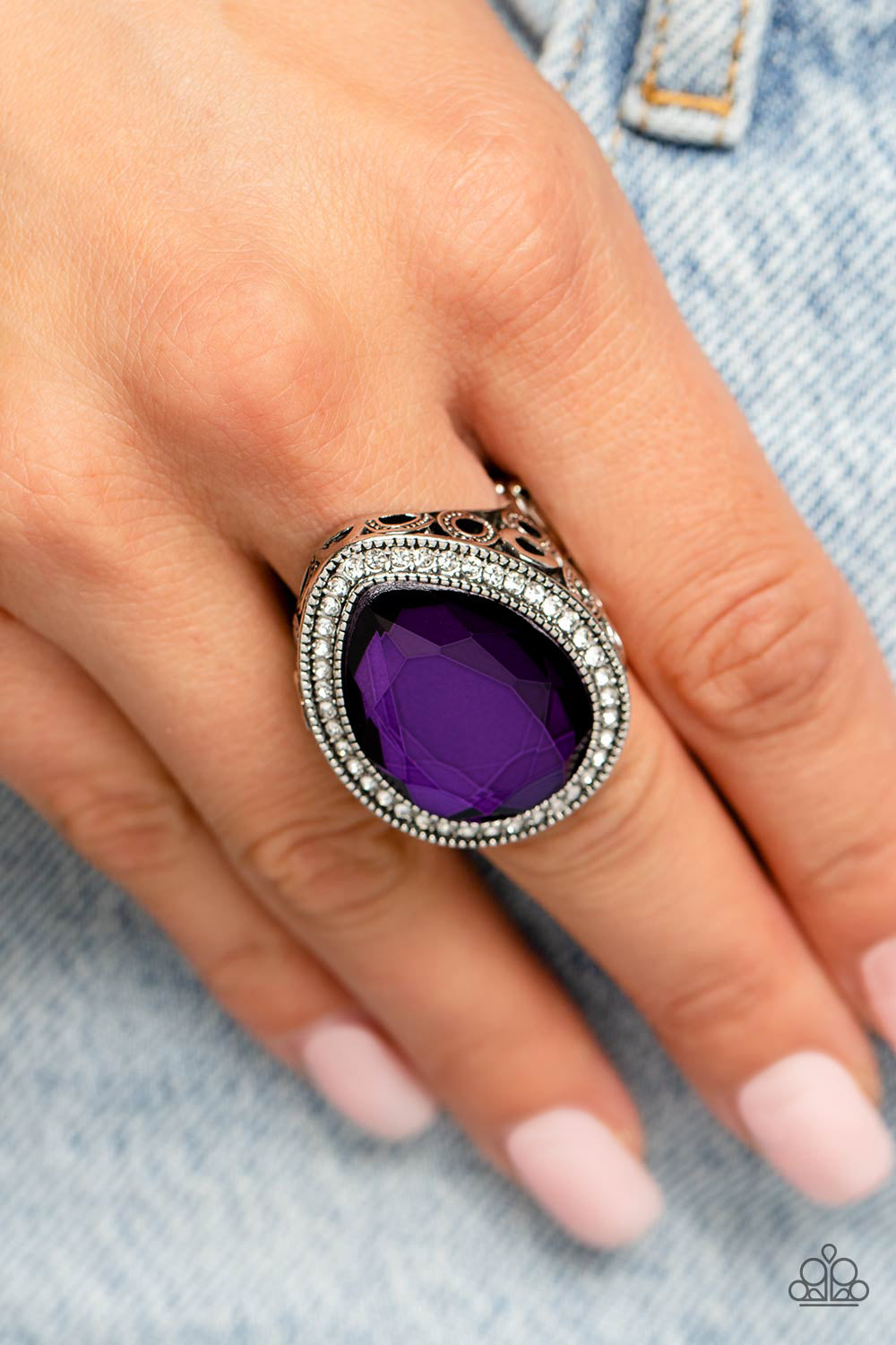 An oversized purple teardrop gem is nestled inside a silver teardrop frame encrusted in dainty white rhinestones. Airy teardrop cutouts decorate each side of the oversized frame, some with subtle texture and others with a high sheen finish. Features a stretchy band for a flexible fit.