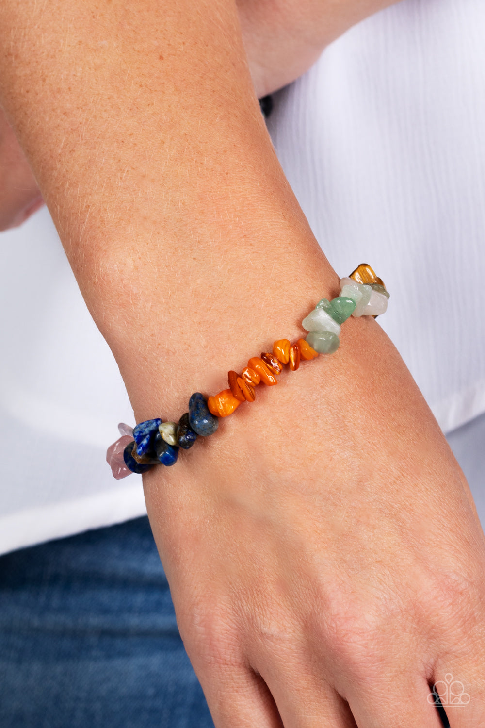 An earthy collection of turquoise, lapis, jade, amethyst, Tiger's eye, orange, gray, and pink pebbles are threaded along a stretchy band around the wrist for a Southwestern finish.
