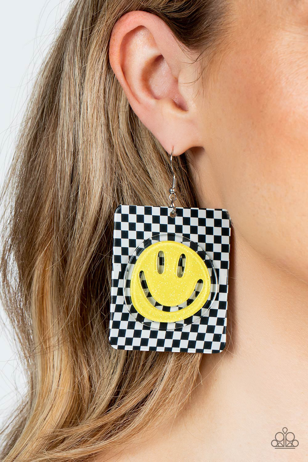 Set against a trendy, checkerboard backdrop, an oversized, sparkly, yellow smiley face stands out for a cheerfully captivating statement piece near the ear. Earring attaches to a standard fishhook fitting.