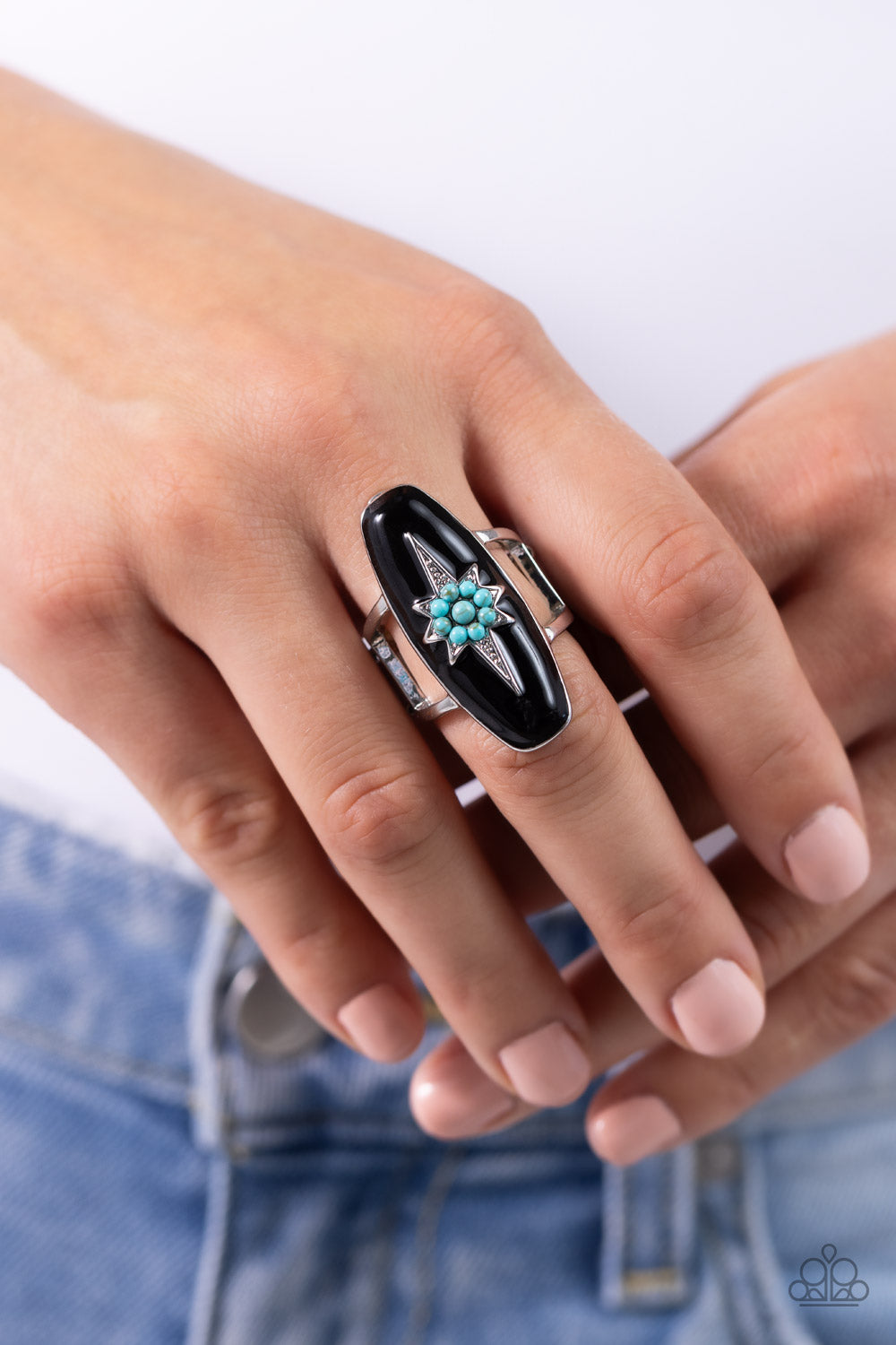 A three-dimensional silver star featuring a turquoise stone flower center is pressed into an elongated black-painted frame atop airy silver bands, creating an earthily stellar centerpiece atop the finger. Features a stretchy band for a flexible fit. As the stone elements in this piece are natural, some color variation is normal.