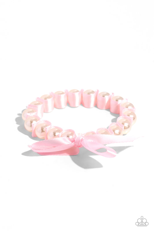 Delicately wrapped in the folds of a baby pink ribbon, gleaming white pearls are infused along an elastic stretchy band around the wrist for a feminine, girly statement.